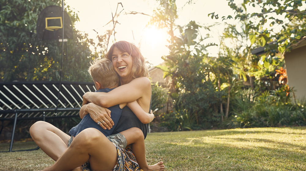 Woman hugging her sun outside on the grass looking very happy